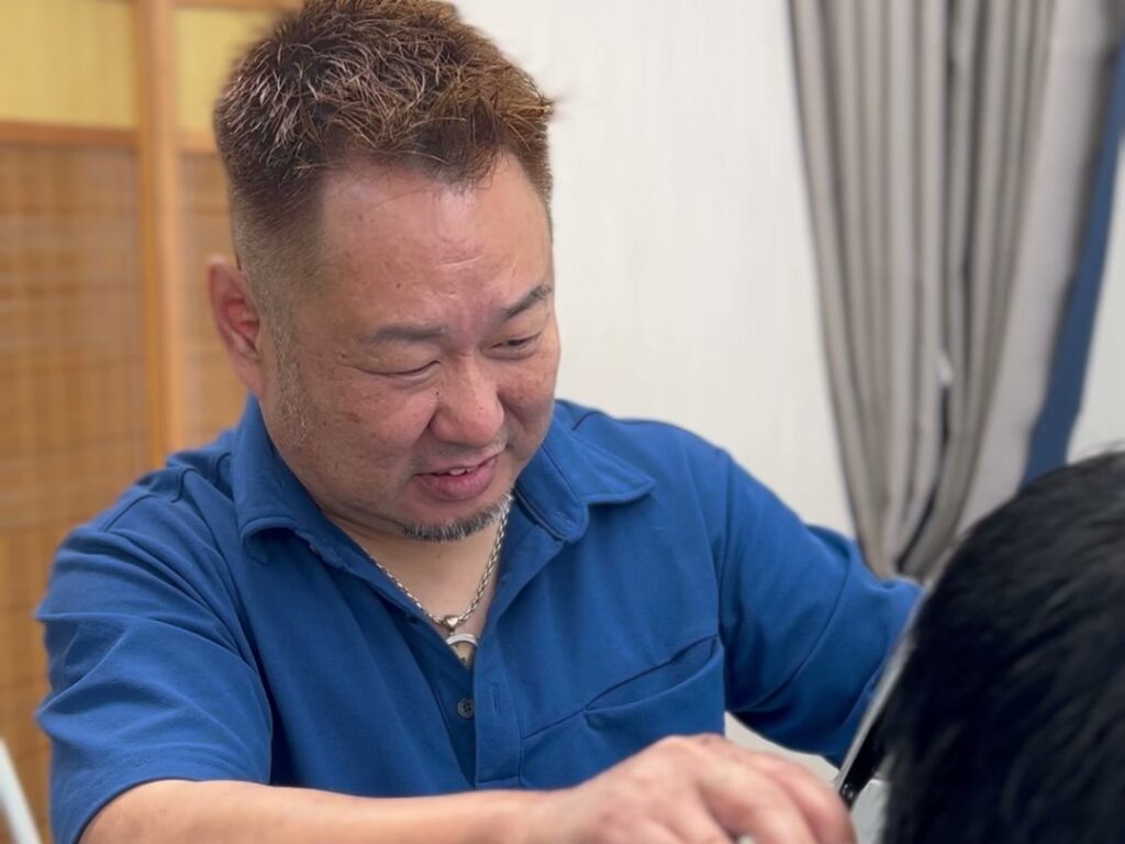 倉敷市児島の理容室のんきで、店長が笑顔で散髪をしている様子